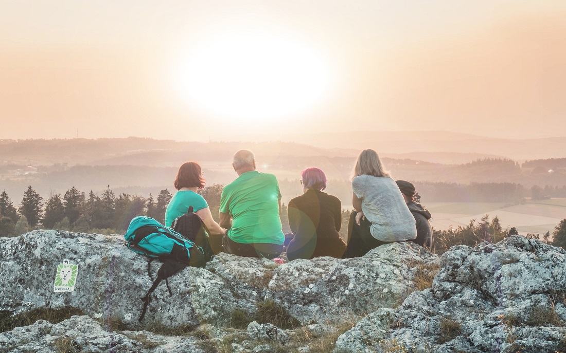 group of people sitting on rock looking at sunset